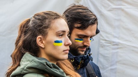 Eine Frau und ein Mann mit aufgemalten ukrainischen Fahnen auf ihren Gesichtern / © Matyas Rehak (shutterstock)