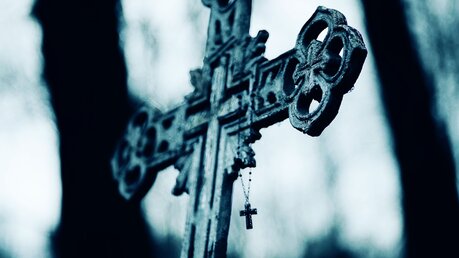 Altes Kreuz auf einem Friedhof, auf dem ein Rosenkranz hängt / © Valeri Vatel (shutterstock)