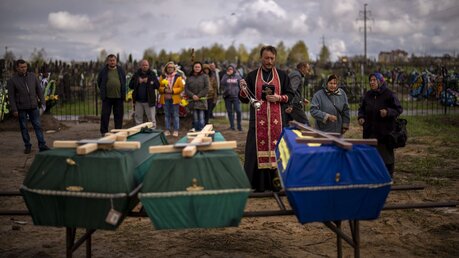 Ukraine, Butscha: Ein Priester segnet drei Verstorbene, die während der russischen Besatzung starben und aus provisorischen Gräbern in Butscha exhumiert wurden / © Emilio Morenatti (dpa)