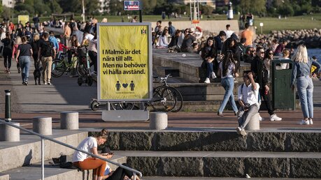 Malmö: Menschen genießen das warme Abendwetter hinter einem Schild, das sie darauf hinweist, Abstand zu halten.  / © Johan Nilsson (dpa)