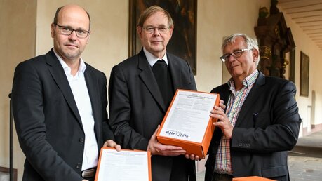 Michael Schrom (l.) und Thomas Seiterich (r.) übergeben die Petition an Pater Hans Langendörfer (m.) / © Harald Oppitz (KNA)