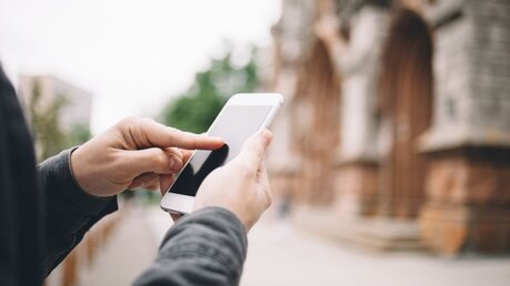 Mit dem Smartphone vor der Kirche / © SG SHOT (shutterstock)