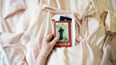 Patientin hält Karten mit Heiligenbildern in ihrer Hand / © Corinne Simon (KNA)
