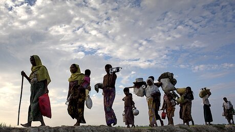 Rohingya-Flüchtlinge gehen mit ihrem Gepäck über ein Reisfeld / © Km Asad (dpa)