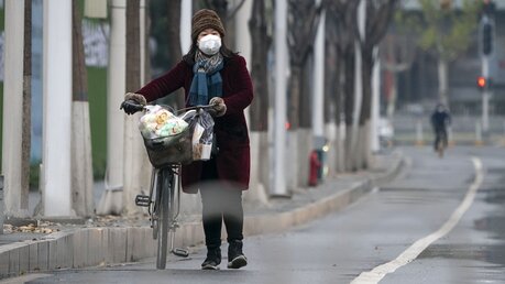 Eine Frau mit Mundschutz schiebt ihr Fahrrad auf einer Straße / © Xiong Qi (dpa)