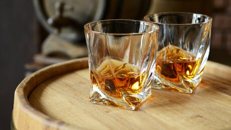 Zwei Whisky-Gläser stehen auf einem Holzfass.  / © Africa Studio (shutterstock)