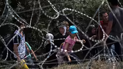 Fl&uuml;chtlinge &uuml;berwinden einen Stacheldrahtzaun an der serbisch-ungarischen Grenze (KNA)