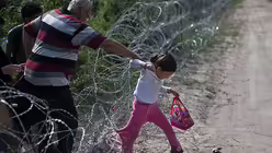 Fl&uuml;chtlinge &uuml;berwinden einen Stacheldrahtzaun an der serbisch-ungarischen Grenze (KNA)