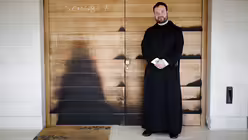 Pater Nikodemus Schnabel vor einer T&uuml;r zum Atrium der Brotvermehrungskirche, die noch Brandspuren aufweist / &copy; Corinna Kern (dpa)