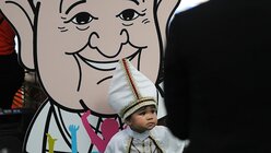  Ein als Papst verkleidetes Kind steht vor einer Comicfigur von Papst Franziskus im Saint Louis Hospital / © Manish Swarup (dpa)