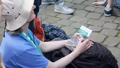 Eine Frau lauscht der Eröffnungsveranstaltung. Sie sitzt inmitten der Menge.  / © Melanie Trimborn (DR)