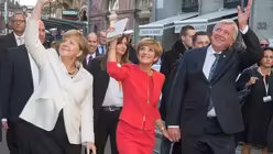 Der hessische Ministerpr&auml;sident und Bundesratspr&auml;sident Volker Bouffier (r), seine Frau Ursula (M) und Bundeskanzlerin Angela Merkel winken am 03.10.2015 in Frankfurt/Main Schaulustigen zu. / &copy; Boris Roessler (dpa)