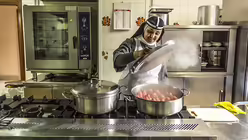 Ordensschwester Gertrude arbeitet in der K&uuml;che am Herd, sie nimmt einen Topfdeckel von einem Topf mit dampfenden Birnen. (KNA)