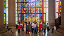 Eine Gruppe Menschen besichtigt die Basilika Notre-Dame-de-la-Paix am 24. November 2019 in Yamoussoukro, Elfenbeinküste. Sie schauen sich ein buntes Kirchenfenster an. / © Francesco Pistilli (KNA)