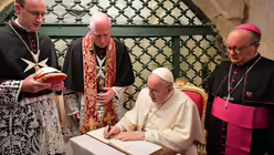 Papst Franziskus schreibt in der Paulusgrotte in Rabat (Malta) in ein Buch. Rechts Charles Jude Scicluna, Erzbischof von Malta / &copy; Vatican Media/Romano Siciliani (KNA)