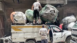 Männer entladen einen mit Müllsäcken gefüllten LKW. / © Manuel Meyer (KNA)
