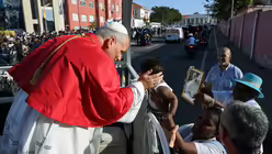 Papst Leo XIV. h&auml;lt seine Hand an den Kopf eines Kleinkindes, das zum Papamobil hochgehalten wird, am 18. April 2026 auf einer Stra&szlig;e in Luanda (Angola). / &copy; Vatican Media/Romano Siciliani (KNA)