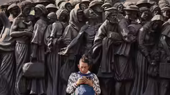 Eine Frau sitzt auf dem Petersplatz neben der Skulptur "Angels Unawares", während die Menschen darauf warten, dem aufgebahrten Papst Franziskus am Sarg im Petersdom die letzte Ehre zu erweisen / © Andreea Alexandru (dpa)