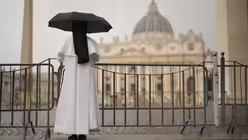 Eine Nonne schützt sich vor dem Regen, während sie die letzte Messe der Kardinäle im Petersdom vor dem Konklave zur Wahl eines neuen Papstes auf dem Petersplatz verfolgt (dpa)