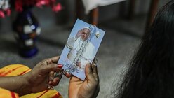 Eine Frau hält ein mit einem Rosenkranz verziertes Bild von Papst Franziskus in ihren Händen / © Turjoy Chowdhury (KNA)