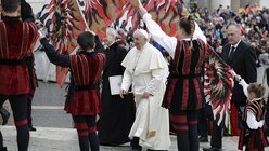 Papst Franziskus geht bei seiner Ankunft zur wöchentlichen Generalaudienz auf dem Petersplatz durch eine Gruppe Fahnenträger. / © Gregorio Borgia/AP (dpa)